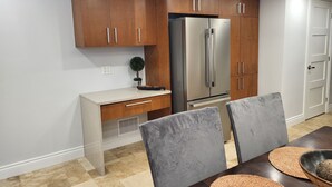 Une cuisine moderne avec des meubles en bois, un réfrigérateur en acier inoxydable, un plan de travail blanc et un coin repas comprenant une table et des chaises.