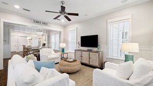 A spacious living room with a ceiling fan, a television, and a dining area with a chandelier.
