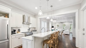 A modern kitchen with white cabinetry, a central island with bar stools, and a dining area with a ceiling fan.