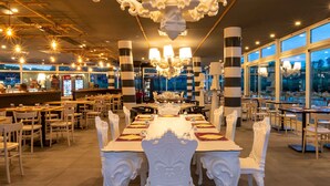 En rummelig restaurant med et langt spisebord, hvide stole og en lysekrone.