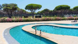 Ein Pool mit geschwungener Form, umgeben von einer begrünten Anlage mit Bäumen und blühenden Pflanzen.