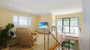 A spacious living room with a beige sofa, a television displaying a beach scene, and a balcony with a view of the outdoors. - Mariners Mark 4 - Your Ultimate Getaway in Hawks Nest (Hawks Nest)