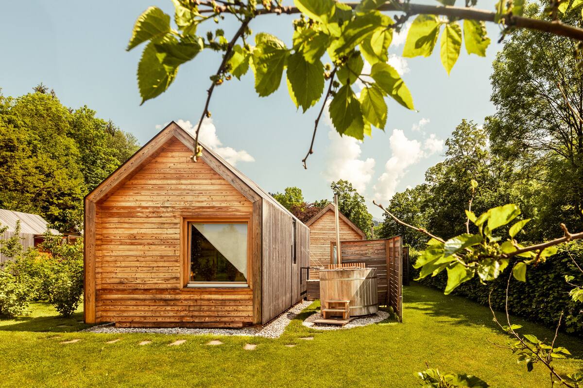 A wooden cabin with a large window and a hot tub in the yard.
