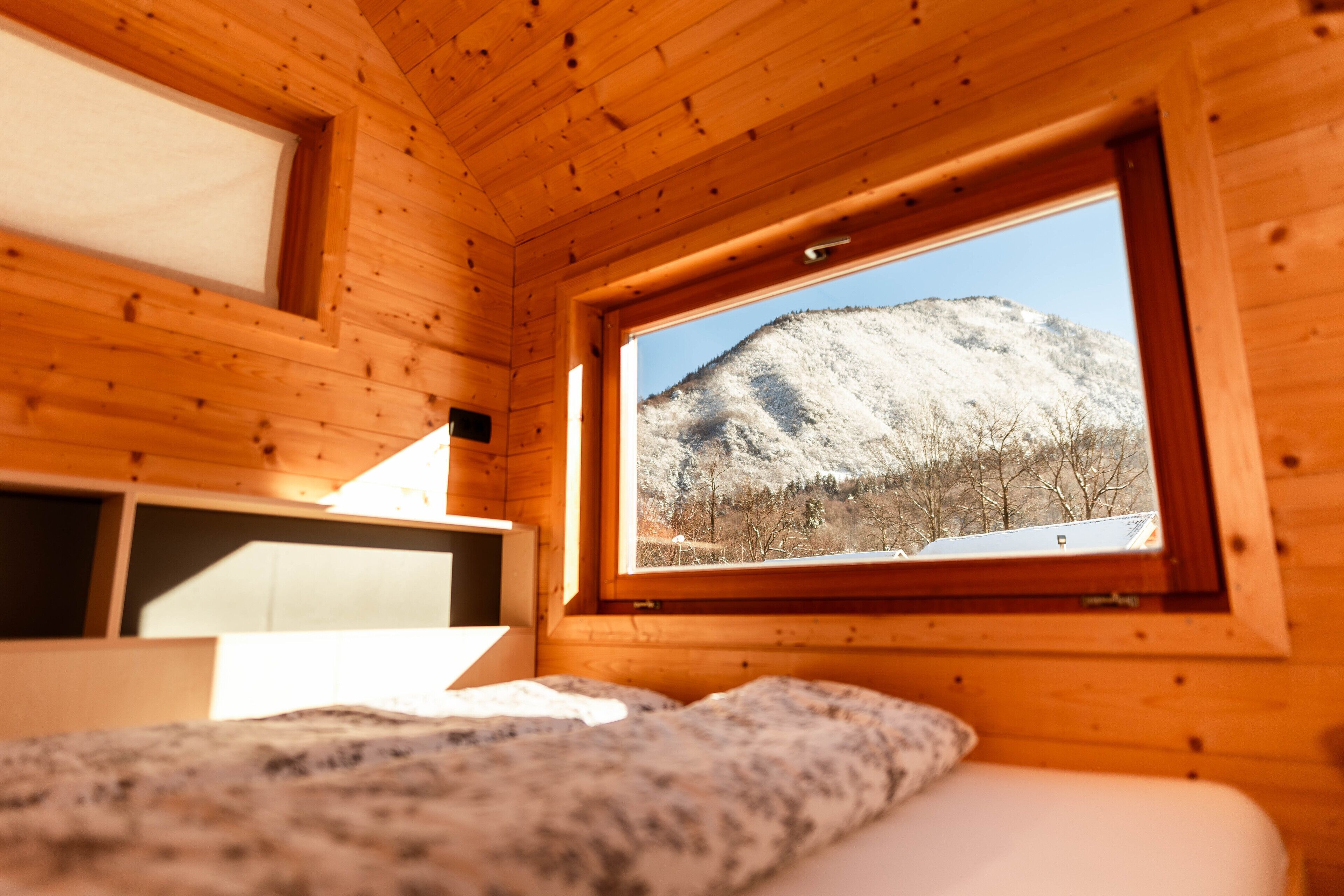 A wooden cabin room with a bed, a window with a view of a snow-covered mountain, and a small desk area.
