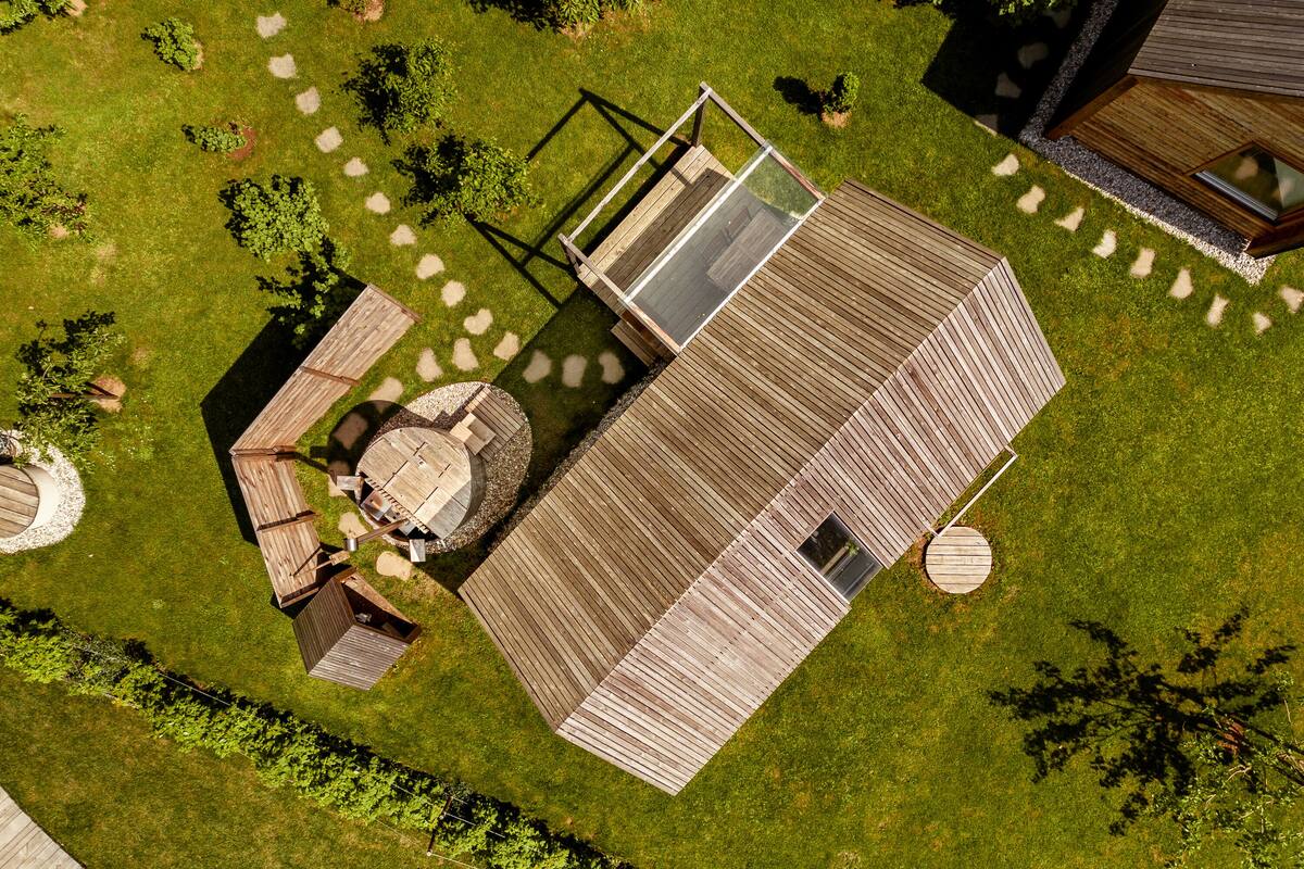 An aerial view of a wooden deck with a glass enclosure, surrounded by a well-maintained lawn and garden.