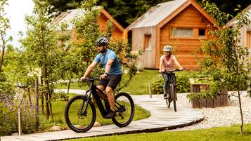 Dois ciclistas em uma trilha de madeira com cabanas de madeira ao fundo.