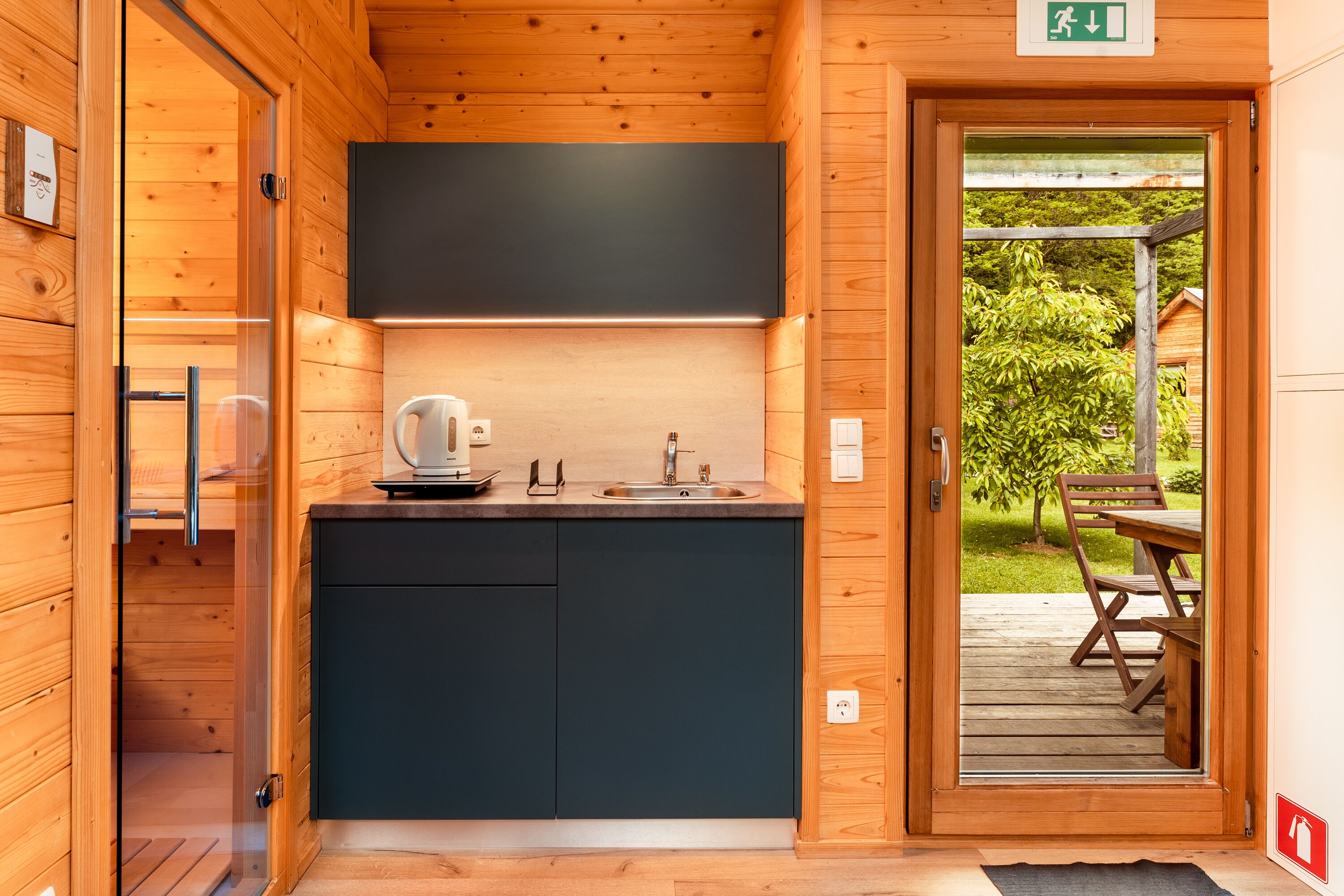 Una cabaña de madera con una zona de cocina que incluye un fregadero, un hervidor y armarios.
