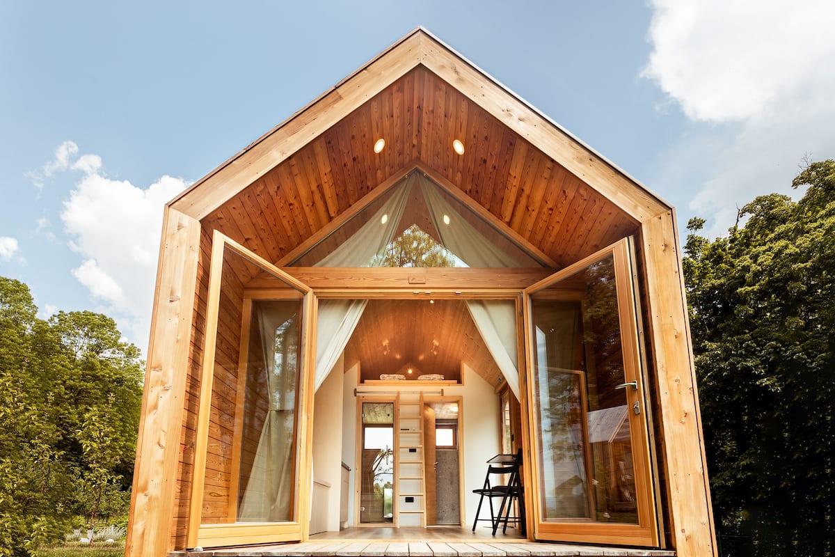 A wooden cabin with a triangular roof, large glass windows, and a wooden deck.