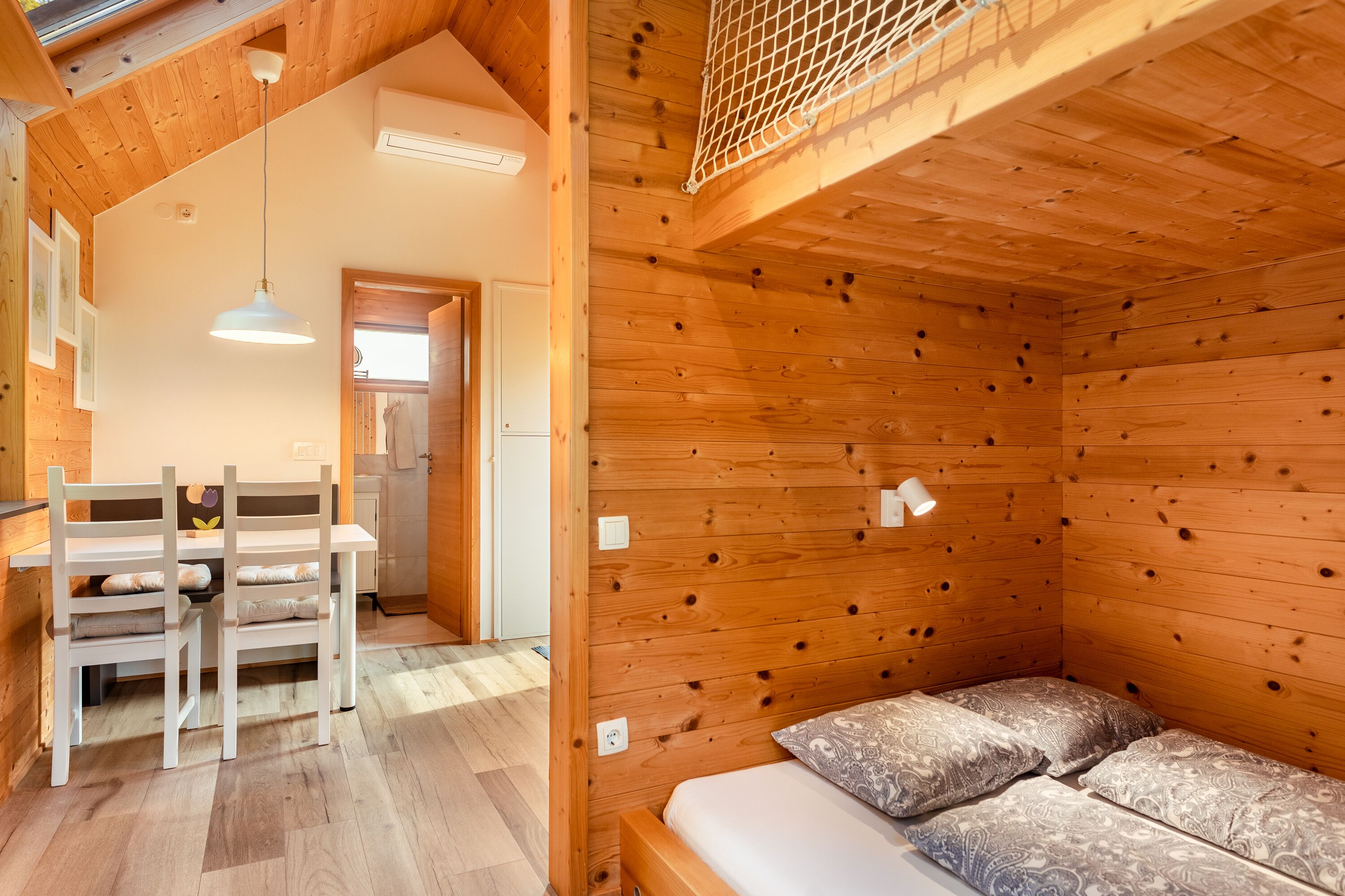 A cozy wooden cabin interior with a bed, a dining table with chairs, and a hanging light fixture.