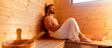 A person sitting in a wooden sauna with a wooden bench and a small wooden bowl.