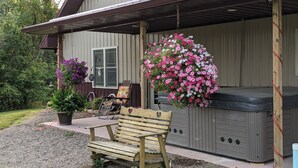 A wooden bench, a hot tub, and a hanging flower basket in front of a house with a porch.