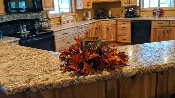 A kitchen with wooden cabinets, granite countertops, a black microwave, and a decorative centerpiece of autumn leaves.