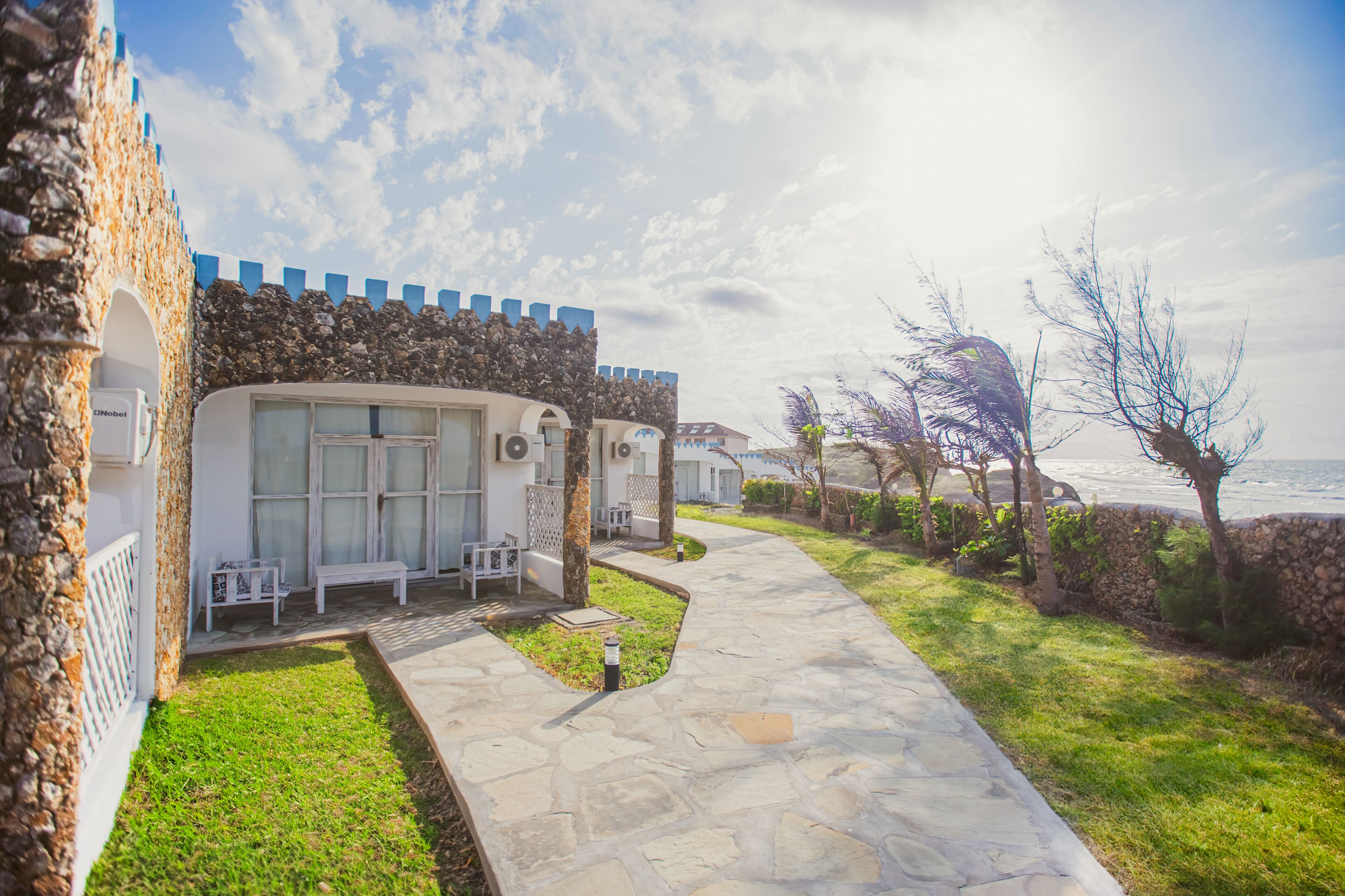 A coastal hotel with stone walls, a paved walkway, and outdoor seating areas.