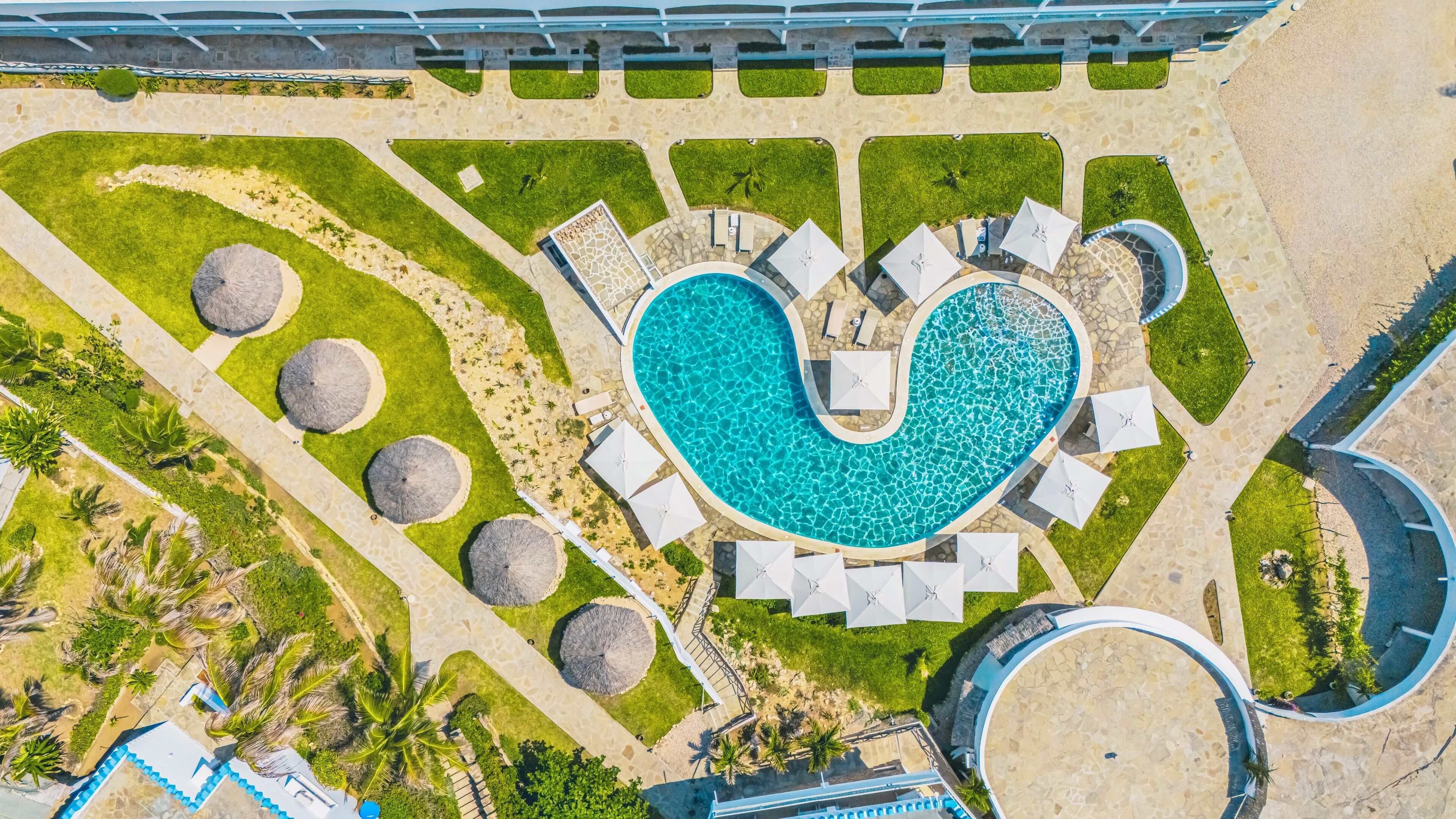 Vue aérienne d’un complexe hôtelier doté d’une piscine en forme de cœur, d’espaces de détente et de palmiers.