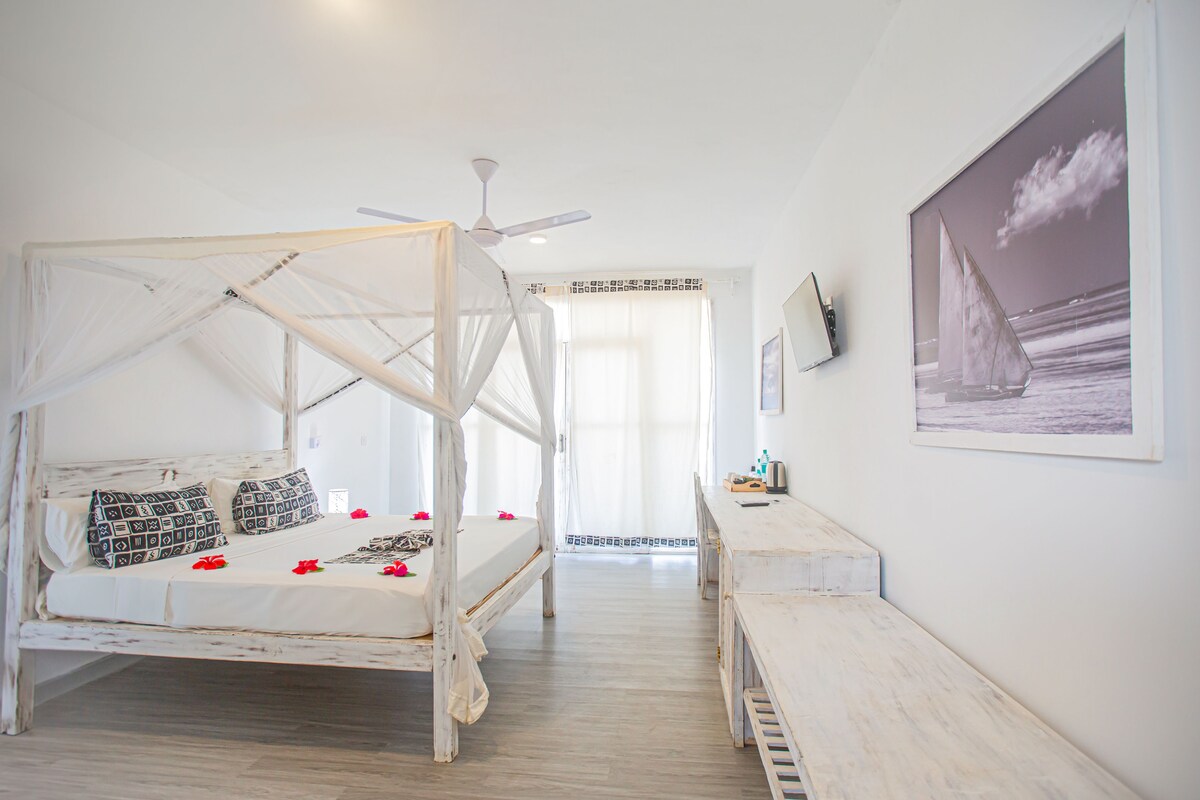 A room with a four-poster bed, a desk, a chair, a ceiling fan, and a framed picture on the wall.