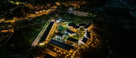 An aerial view of a resort with multiple buildings, a swimming pool, and well-lit pathways.