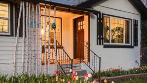 A white house with a wooden porch, a staircase, and a garden with tulips. - Charming 3 Bedroom 1940s Farm House (Lakewood)