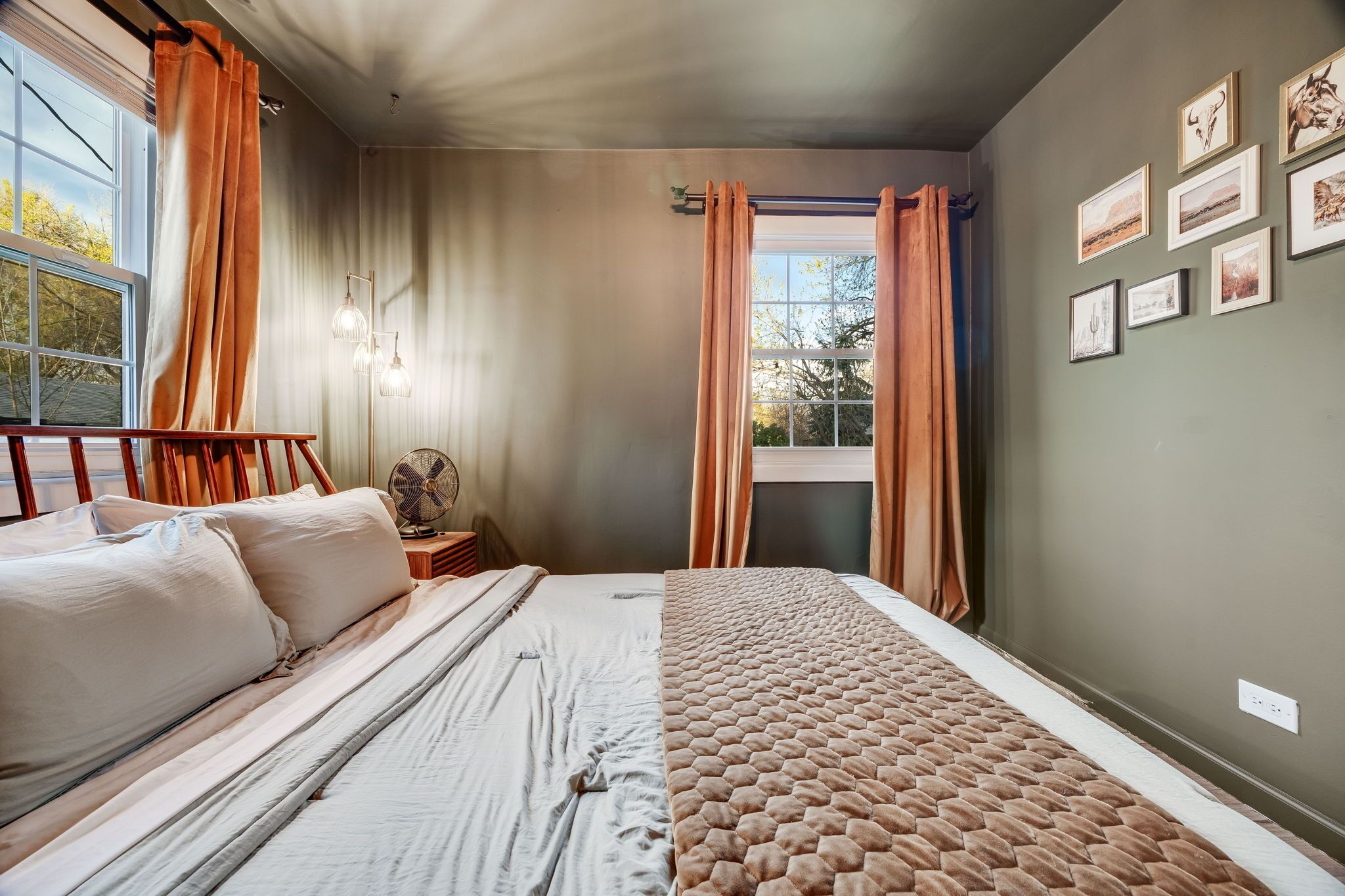 A bedroom with a bed, a bedside table, a fan, and a window with curtains.