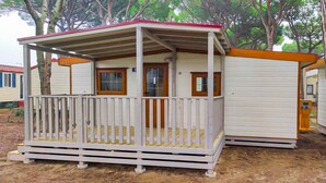 A small, single-story mobile home with a porch and a fenced deck area. - Mobile home with terrace (Cavallino-Treporti)