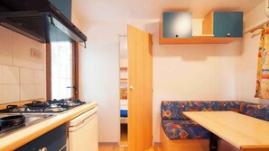 A compact kitchen with a stove, cabinets, and a bench with a table. - Mobile home with terrace (Cavallino-Treporti)