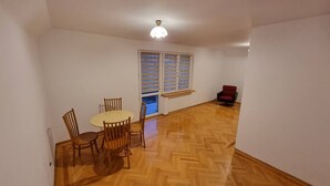 A room with a wooden herringbone floor, a dining table with chairs, a red armchair, and a window with blinds. - Cottage off the beaten track 3 rooms 2 bathrooms

 (Kraków)