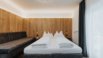 Ein modernes Hotelzimmer mit einer Wandpaneele aus Holz, einem großen Bett mit weißer Bettwäsche, einer dunklen Couch und einem Nachttisch mit Lampe.