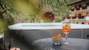 A hot tub, a glass with a drink, and a bowl of chips on an outdoor table with a mountain view. - Hotel Bischofhof - Bistro Jasmin (Chiusa)