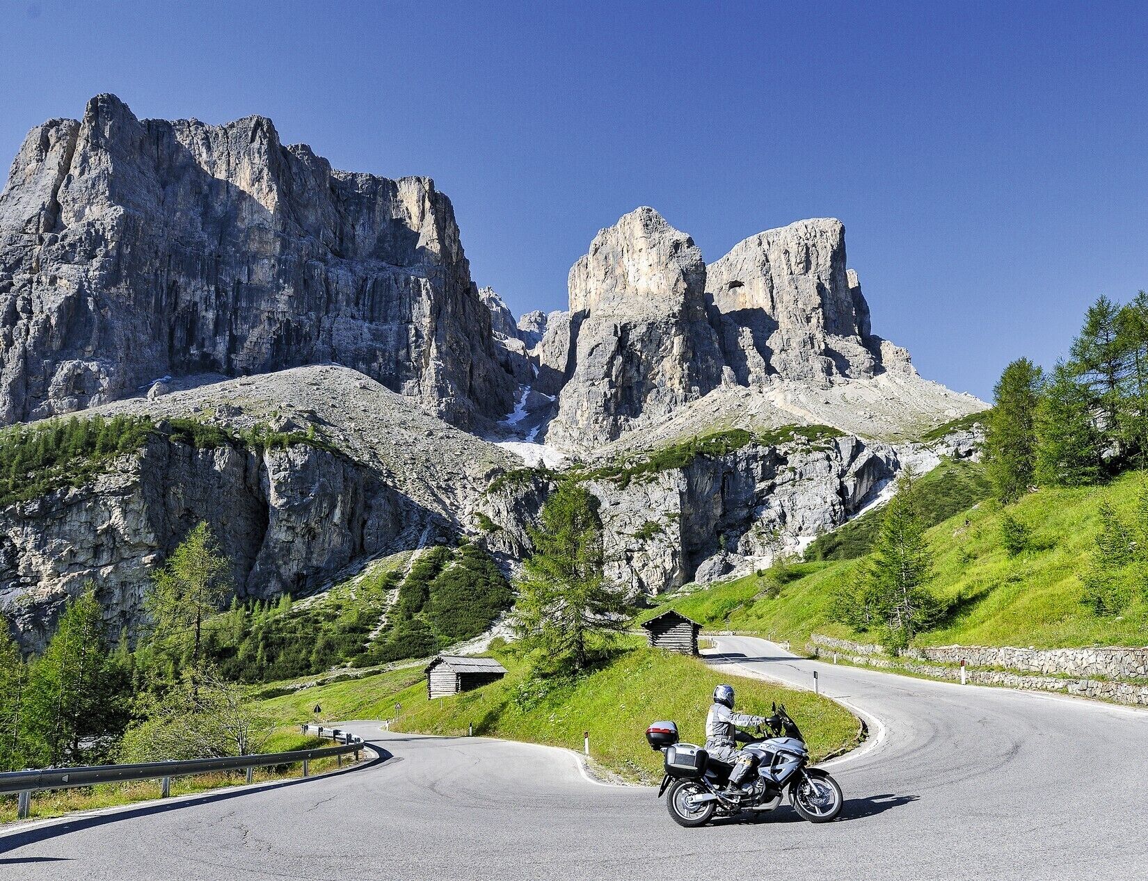 A mountain road with a motorcyclist, rocky cliffs, and a small building.