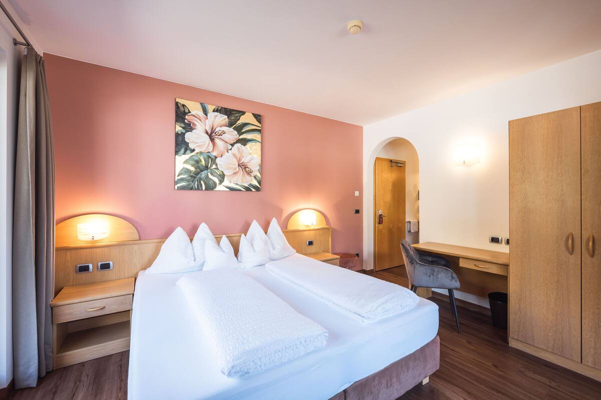 Een hotelkamer met een groot bed, twee nachtkastjes, een bureau, een stoel en een kledingkast.