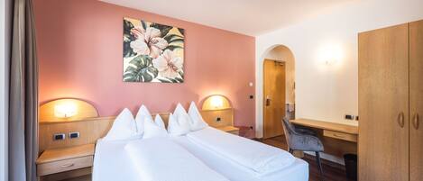 A hotel room with a large bed, two bedside tables, a desk, a chair, and a wardrobe.
