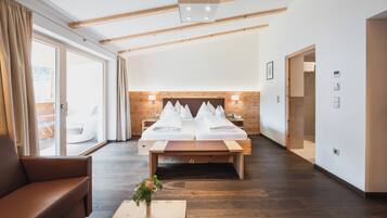 A hotel room with a large bed, wooden beams, a sofa, and a view through the glass door.