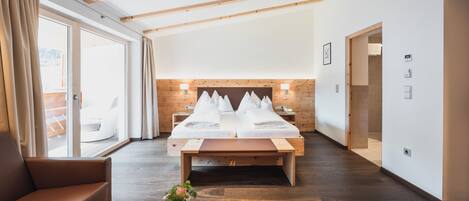 Een hotelkamer met een groot bed, houten balken, een bank en uitzicht door de glazen deur.
