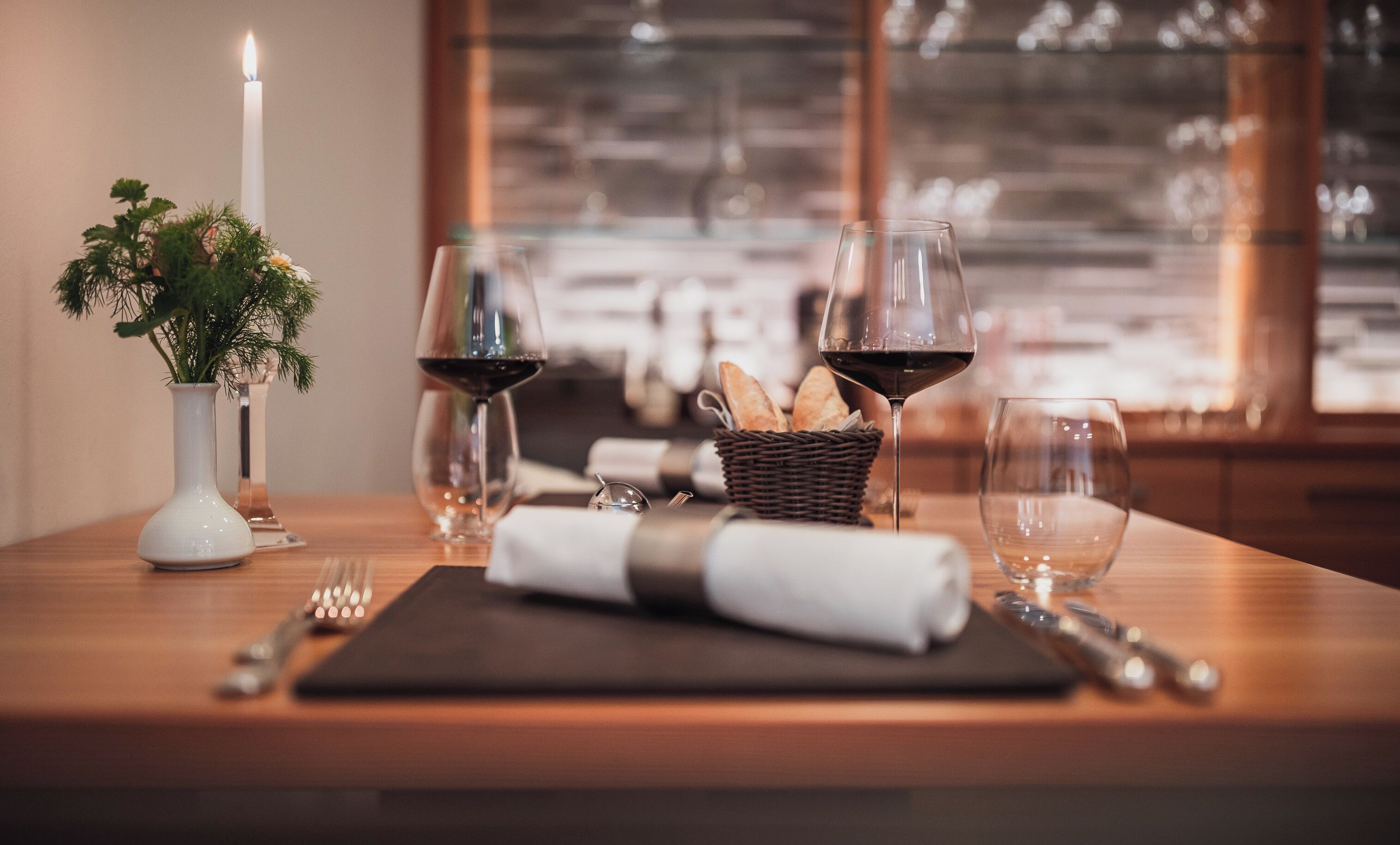 Una mesa de comedor con copas de vino, una vela y una cesta de pan.