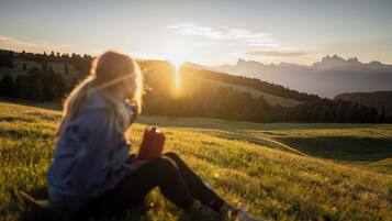 En person sitter på gräset med en vacker utsikt över berg och en solnedgång i bakgrunden.