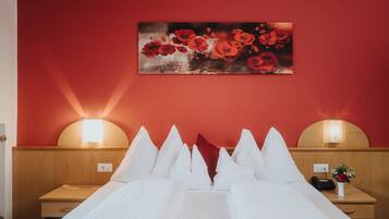 Une chambre d’hôtel avec un mur rouge, un lit recouvert de draps blancs, deux tables de chevet avec des lampes et un tableau représentant des fleurs rouges.