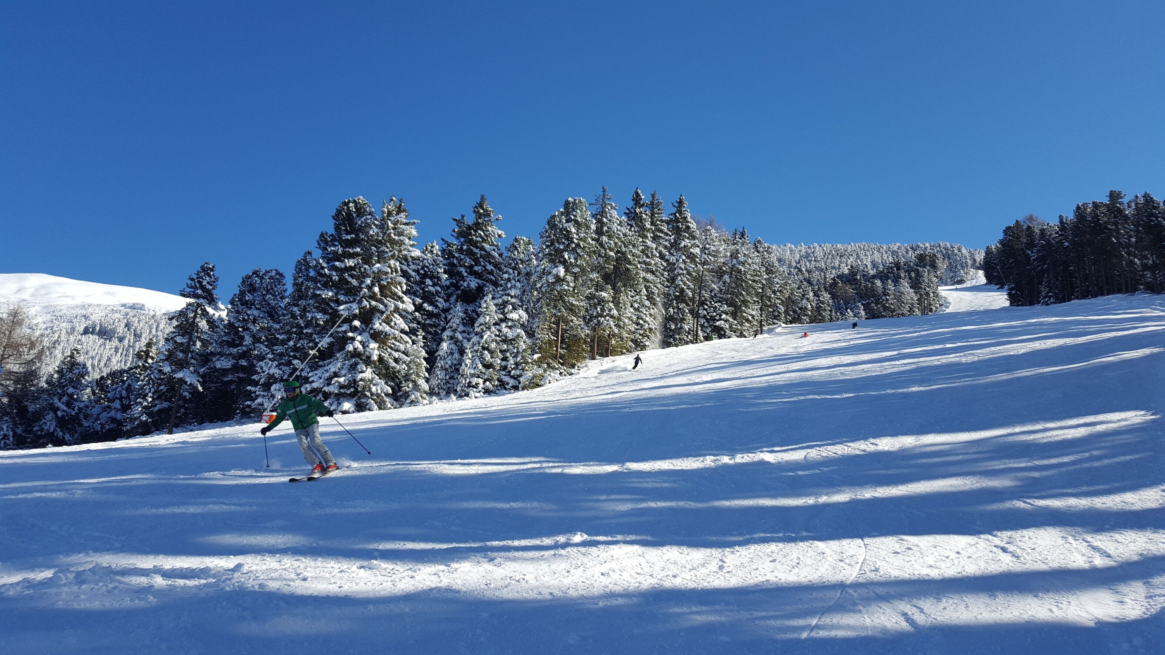 Pista de esqui coberta de neve, com árvores e um céu azul claro.