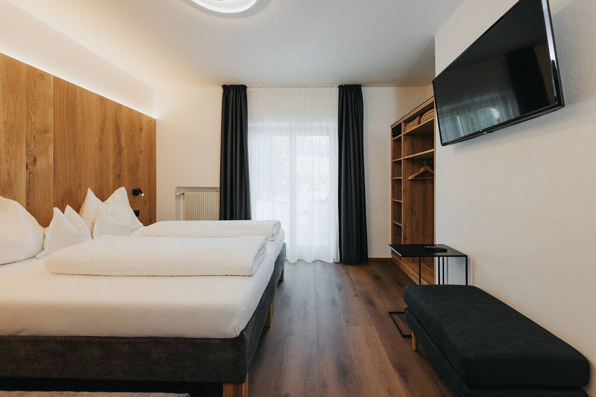 Een hotelkamer met een bed, een bankje, een televisie en een kledingkast.