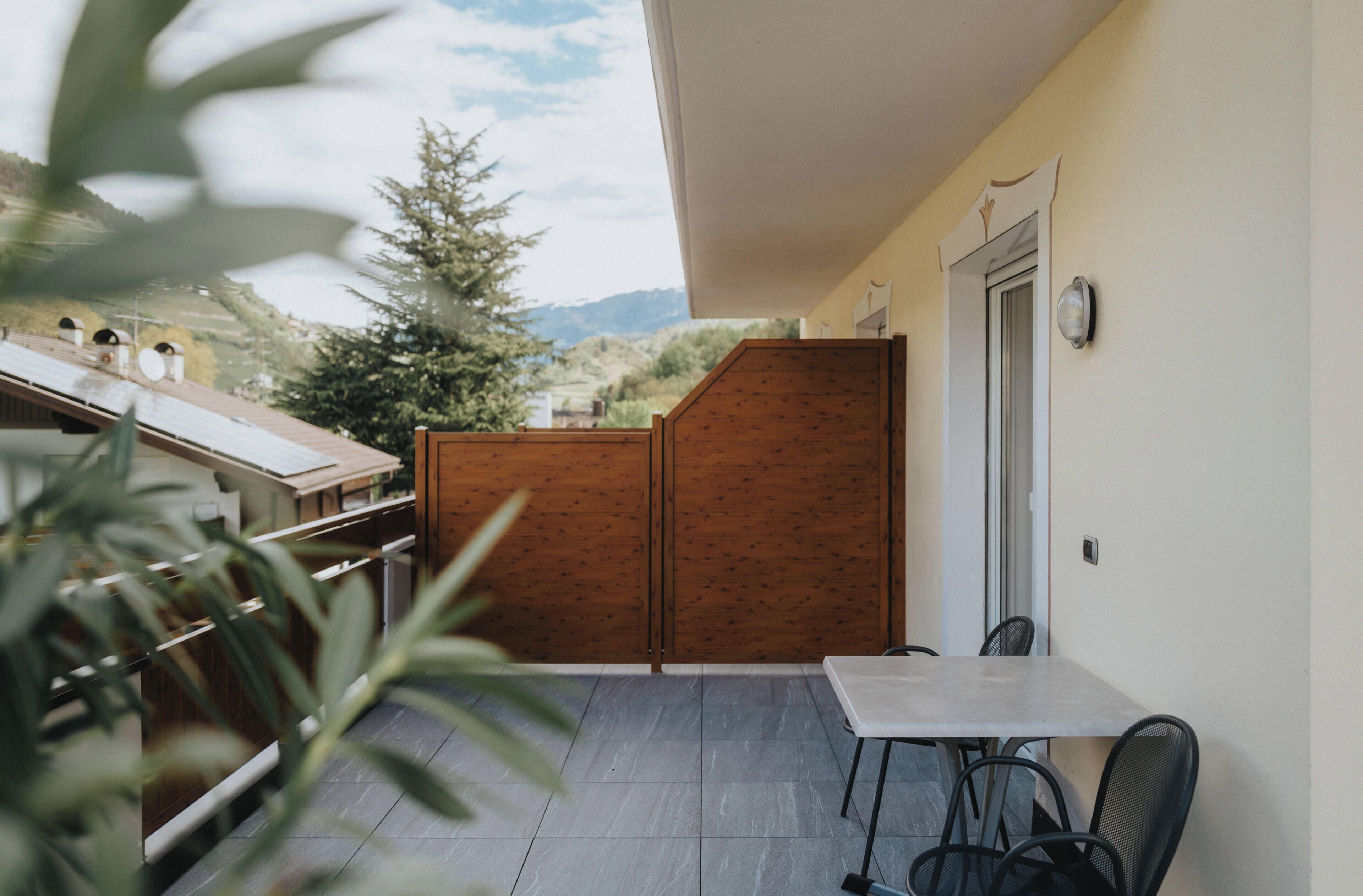 A balcony with a table and chairs, a wooden partition, and a view of a mountain.