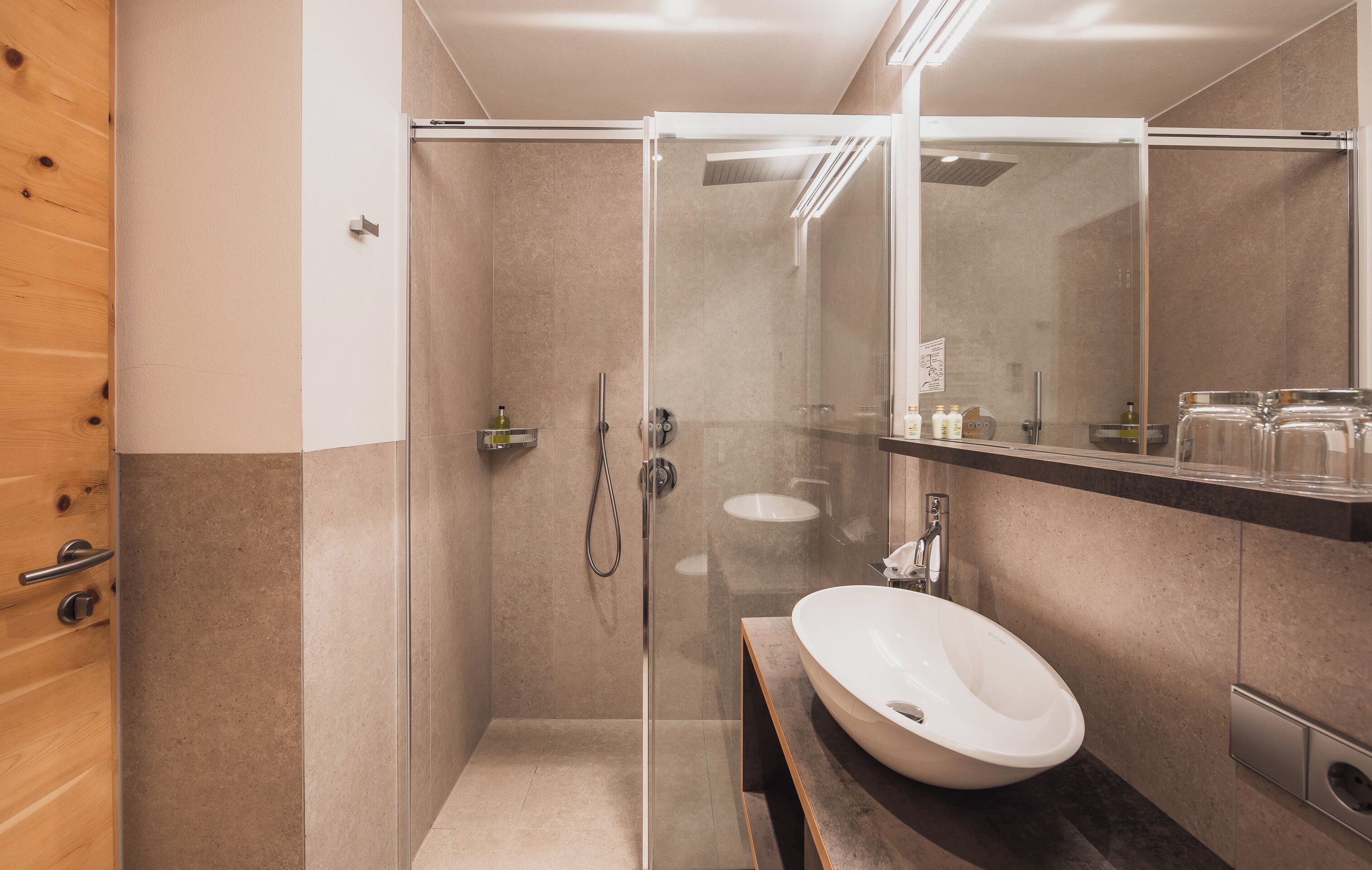 A modern bathroom with a glass-enclosed shower, a white sink, and a large mirror.