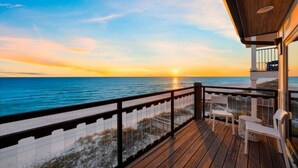 Une terrasse en bois avec une balustrade donnant sur l’océan au coucher du soleil.