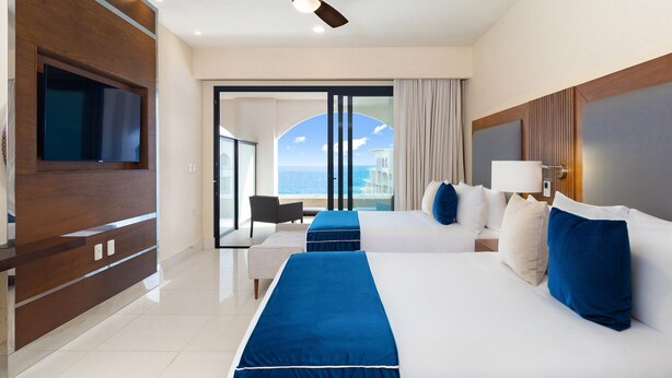 Ein Hotelzimmer mit einem großen Bett, einem Fernseher, einem Deckenventilator und Blick auf den Ozean.