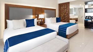 Ein Hotelzimmer mit zwei Betten, einer Bank, einem Holzkopfteil, einem Nachttisch mit Lampe und einem durchgehenden Türspalt einsehbarer Badezimmer.