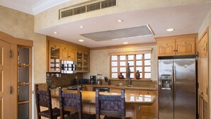 A kitchen with wooden cabinets, a stainless steel refrigerator, and a bar area with stools. - One Bedroom Suite (Cabo San Lucas)