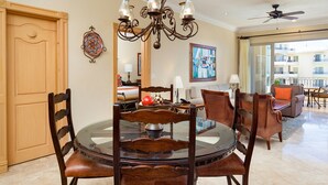 A dining area with a round glass table, wooden chairs, a chandelier, and a view of the outside balcony. - One Bedroom Suite (Cabo San Lucas)