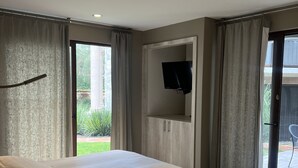 Un dormitorio moderno con una cama grande, un televisor de pantalla plana en la pared y una puerta corrediza de vidrio que da a un espacio al aire libre.
