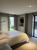 Un dormitorio moderno con una cama grande, un televisor de pantalla plana en la pared y una puerta corrediza de vidrio que da a un espacio al aire libre.