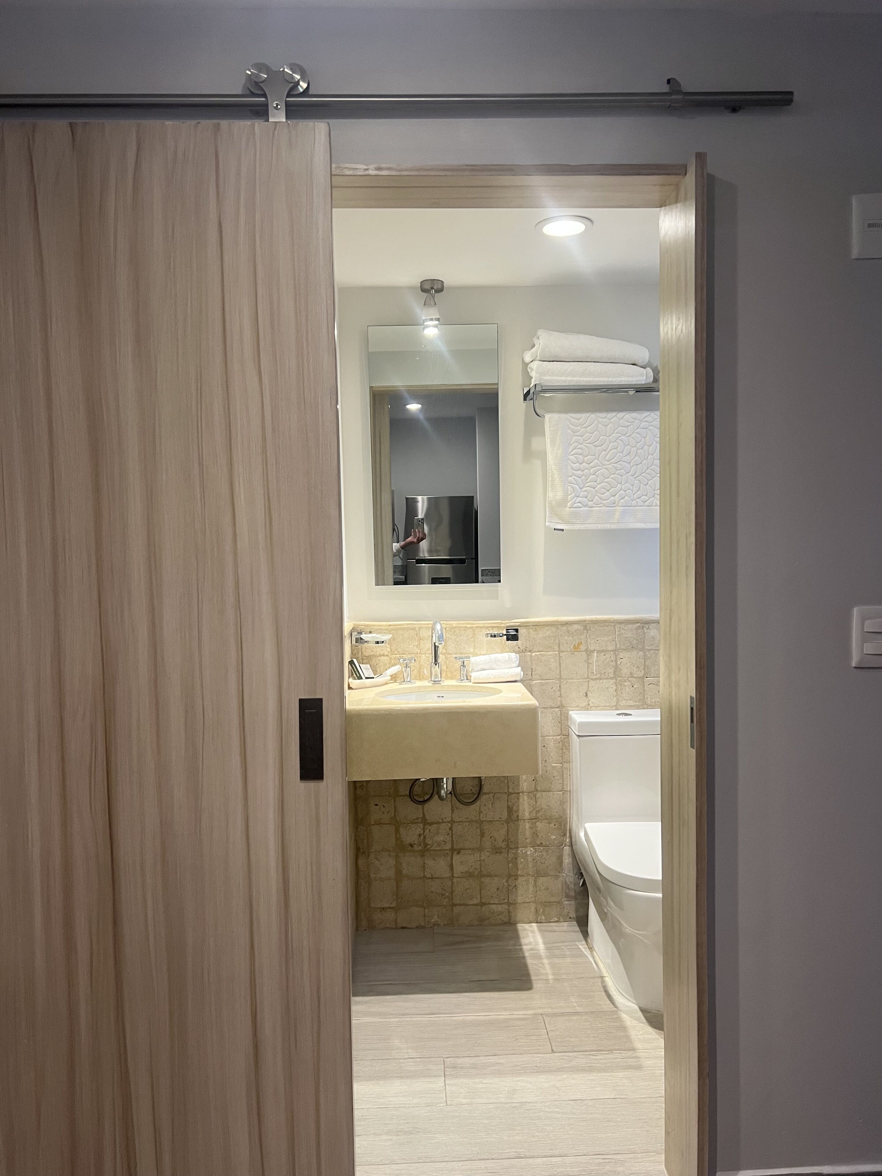 A modern bathroom with a wooden door, a sink, a mirror, and a bathtub.