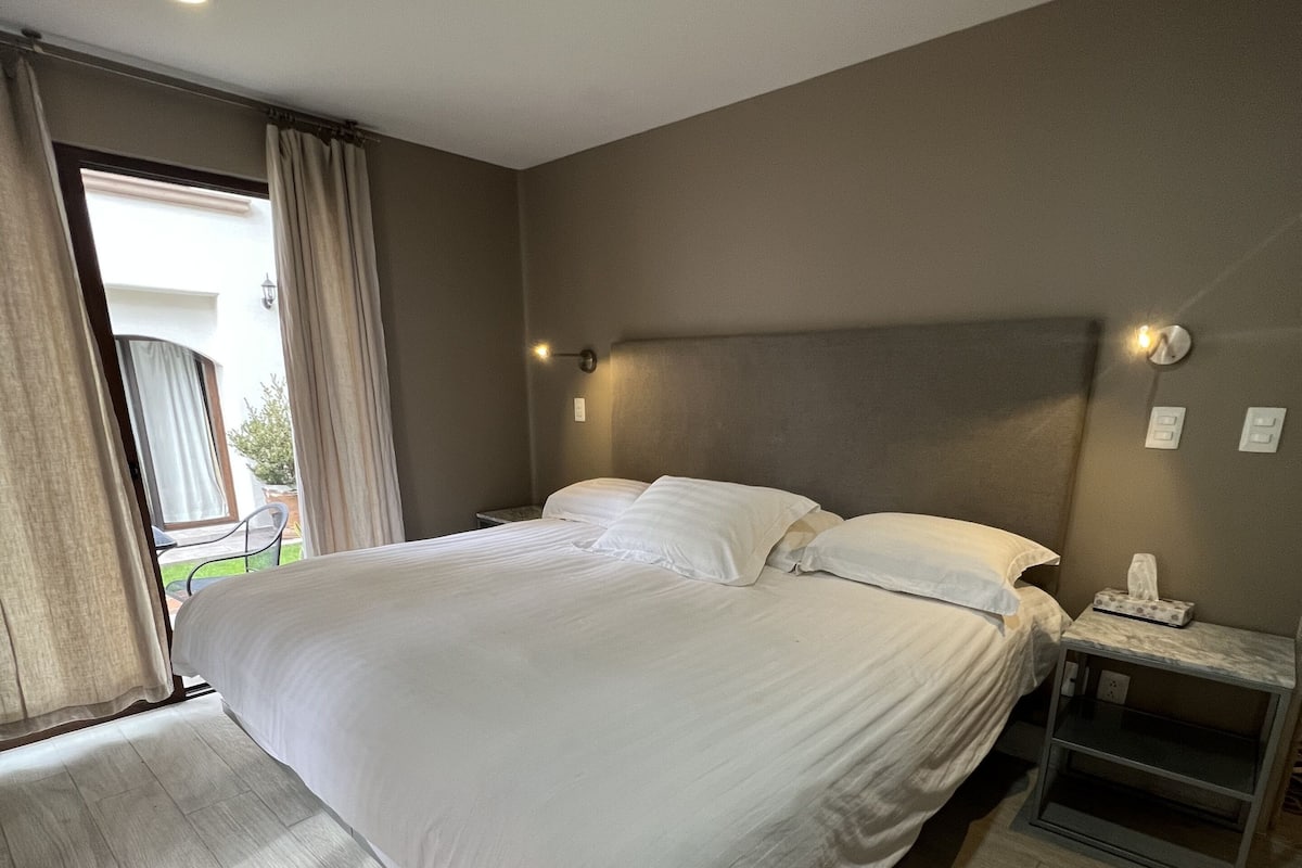 Un dormitorio moderno con una cama grande, una mesita de noche con lámpara y vistas al exterior a través de una ventana.