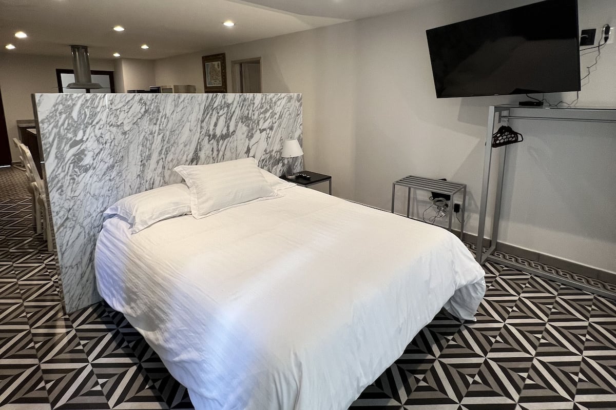 Habitación de hotel con una cama grande, cabecera de mármol, televisor de pantalla plana en la pared y suelo estampado.