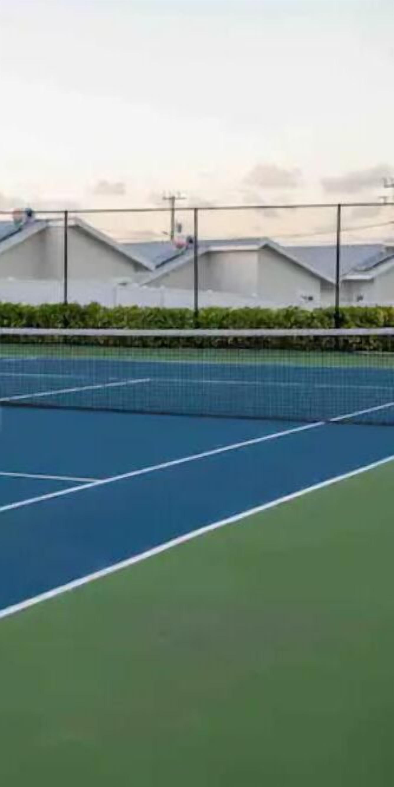 A tennis court with a net, surrounded by a fence and greenery.